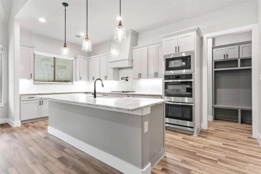 Kitchen featuring light stone counters, sink, light hardwood / wood-style floors, white cabinets, and a kitchen island with sink