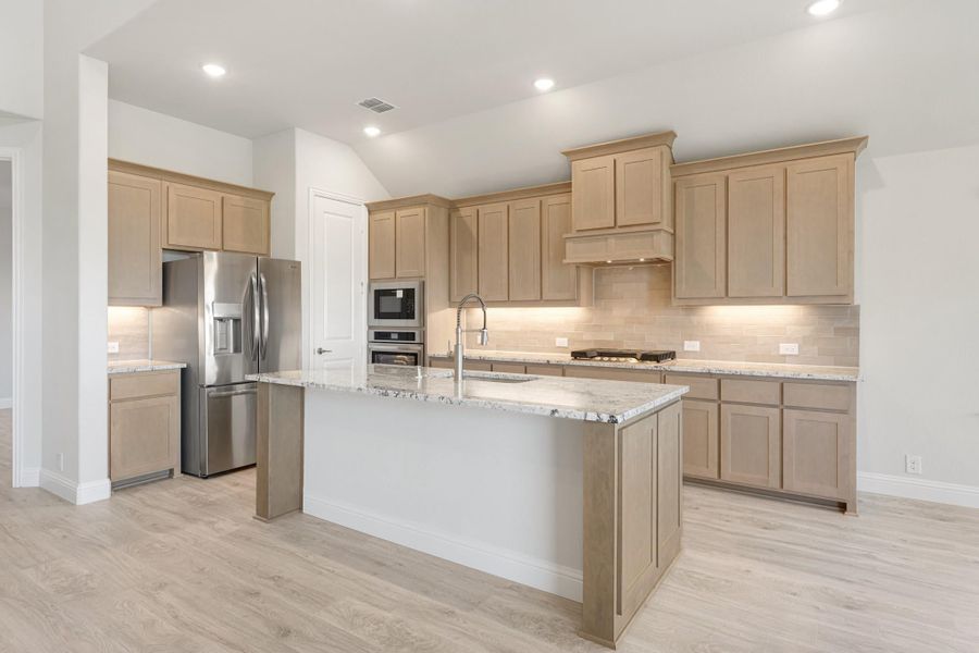 Kitchen with light wood cabinets, granite island with sink, stainless steel appliances, and light hardwood floors