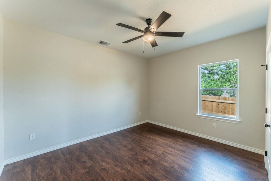 Room featuring wood-finish flooring, a ceiling fan with integrated lighting, and a window with white trim