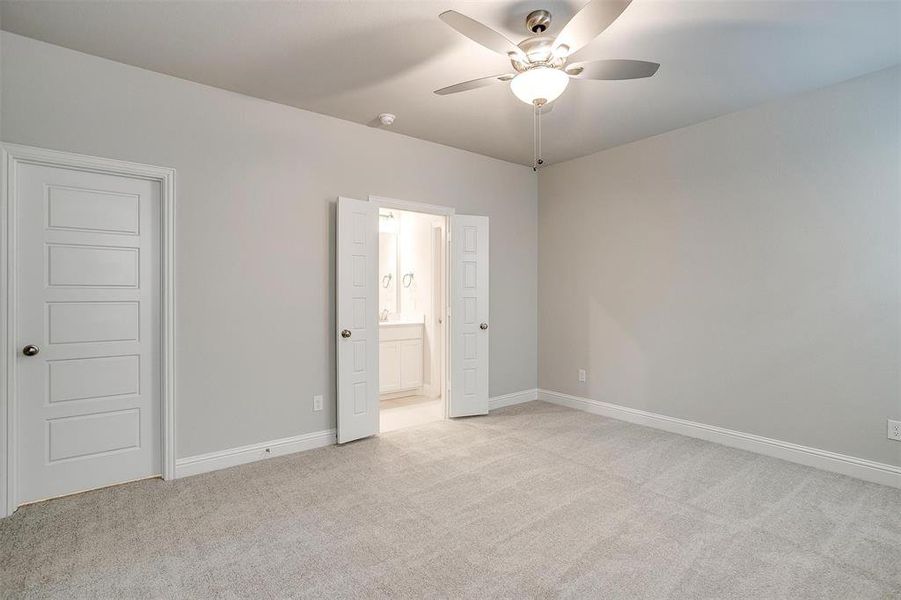 Unfurnished bedroom with ceiling fan, light colored carpet, and ensuite bathroom