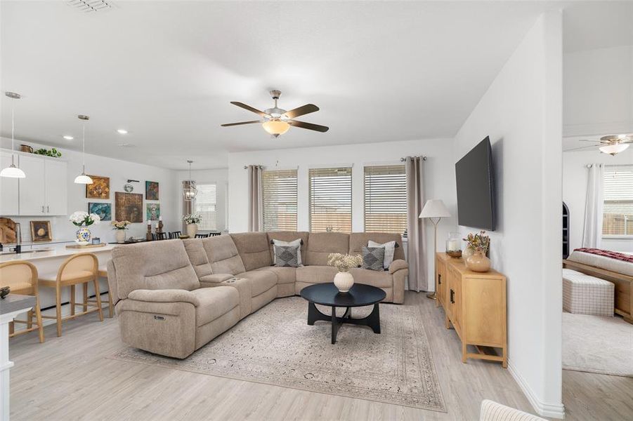 The living area features light-toned flooring, a ceiling fan, and large windows with blinds