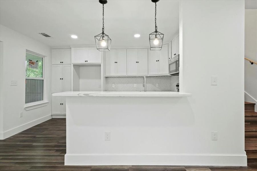 Kitchen with pendant lighting, white cabinetry, backsplash, dark hardwood / wood-style flooring, and sink