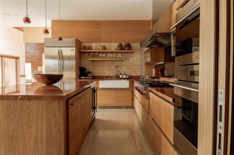 Kitchen featuring range hood, a kitchen island, modern cabinets, appliances with stainless steel finishes, and pendant lighting