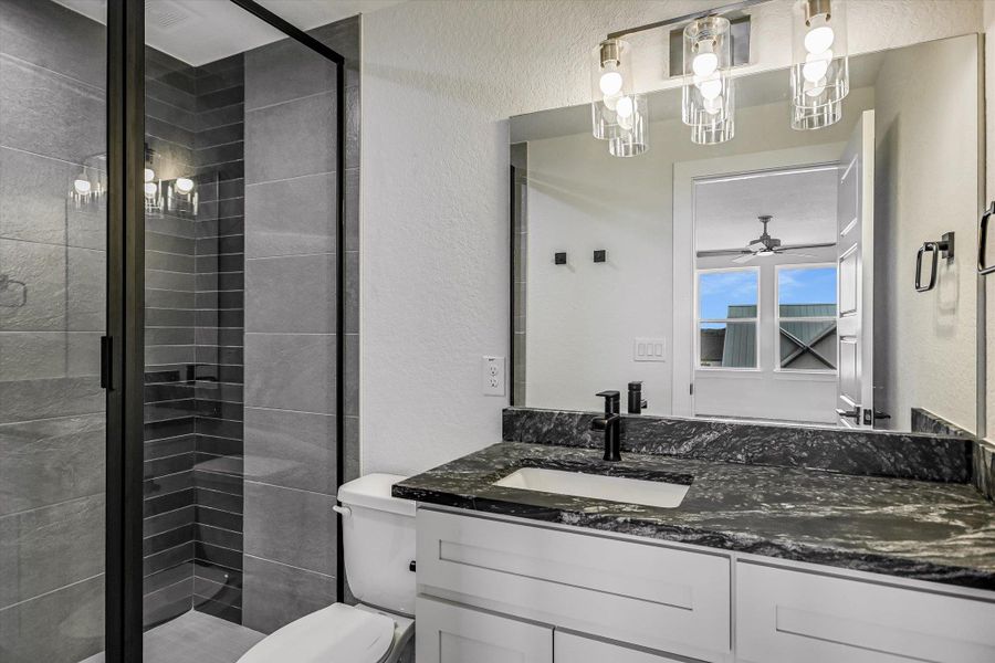 Bathroom with a textured wall, a shower stall, vanity, and ceiling fan