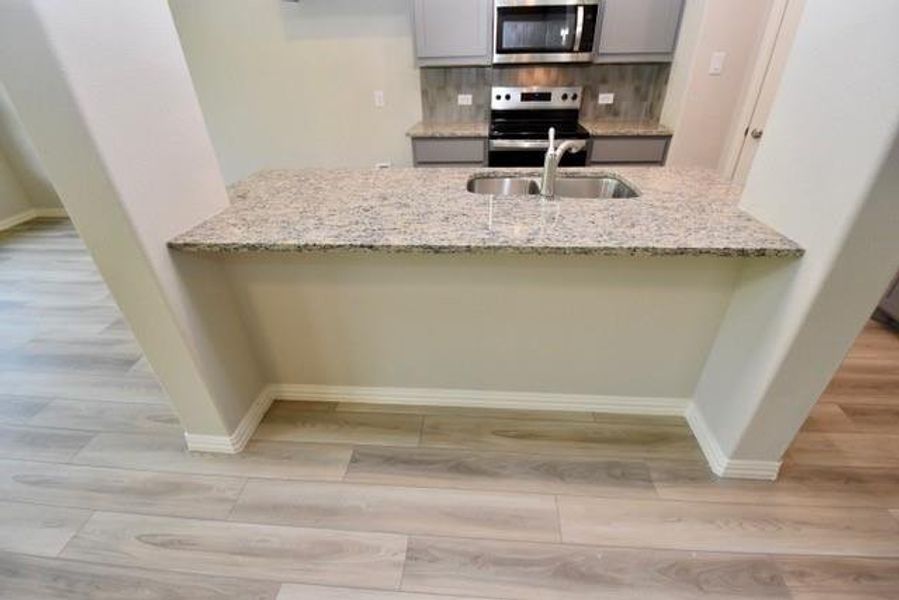 Kitchen with stainless steel appliances, wood finished floors, light stone countertops, and a peninsula