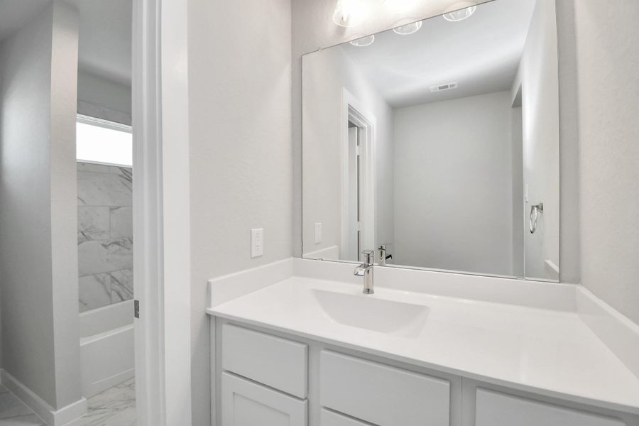Secondary bath features tile flooring, bath/shower combo with tile surround, light stained wood cabinets, beautiful light countertop. Sample photo of completed home with similar floor plan. Actual colors and selections may vary.