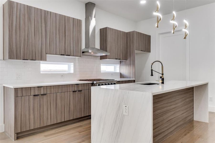 Kitchen with modern cabinets, wall chimney exhaust hood, light wood-style flooring, decorative backsplash, and a kitchen island with sink