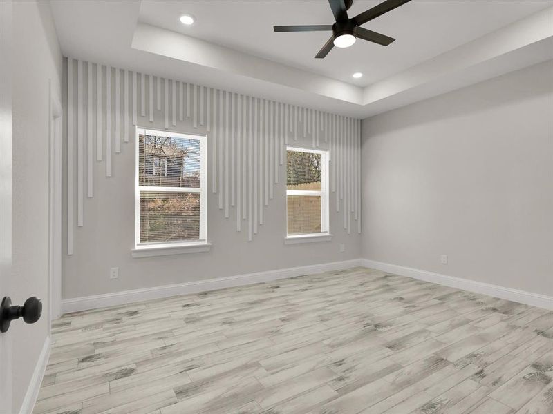 Unfurnished room featuring a tray ceiling, ceiling fan, and light wood-type flooring