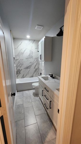 House bath between the upstairs bedrooms. Featuring a sleek vanity with black fixtures, marble-style tile in the shower, and neutral floor tiles. Bright and inviting space with ample lighting.