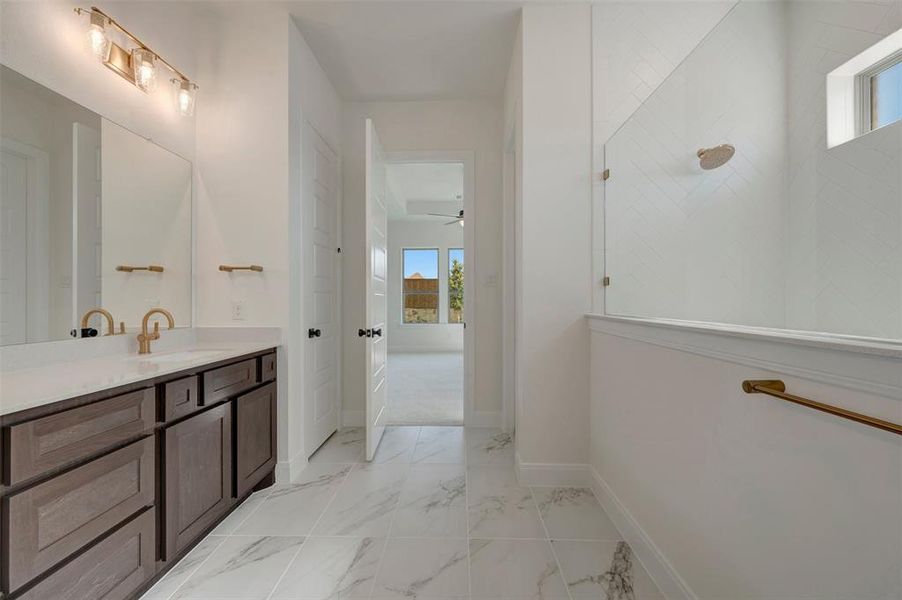 Bathroom featuring a dual vanity with a white countertop and bronze-finish faucets, bronze-finish wall lighting, a large vanity mirror, and marble-look floor tiling Bathroom featuring a dual vanity with a white countertop and bronze-finish faucets, bronze-finish wall lighting, a large vanity mirror, and marble-look floor tiling