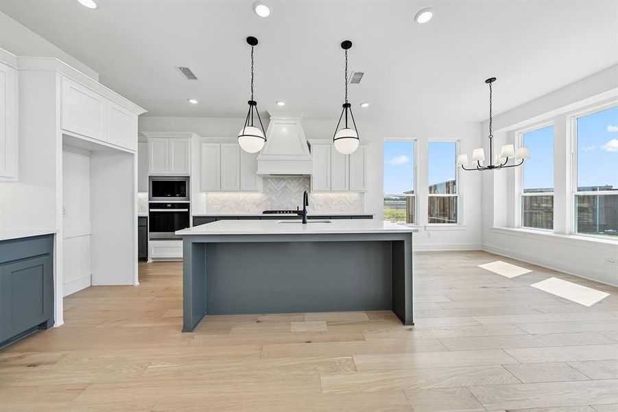 Kitchen featuring backsplash, pendant lighting, white cabinetry, light wood-type flooring, and oven