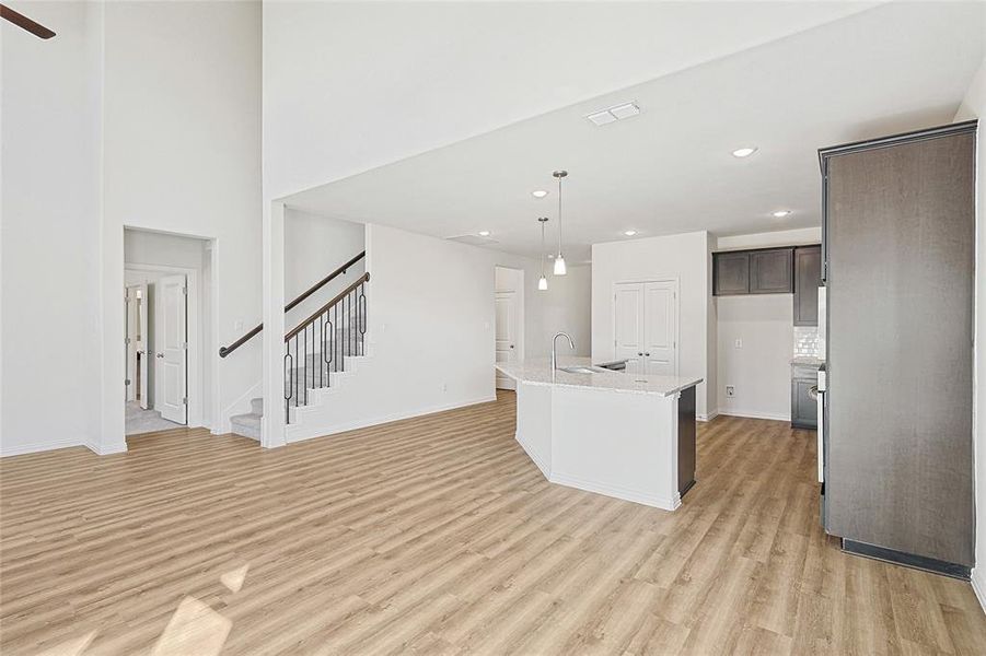 Kitchen with dark brown cabinetry, sink, hanging light fixtures, light hardwood / wood-style flooring, and a center island with sink