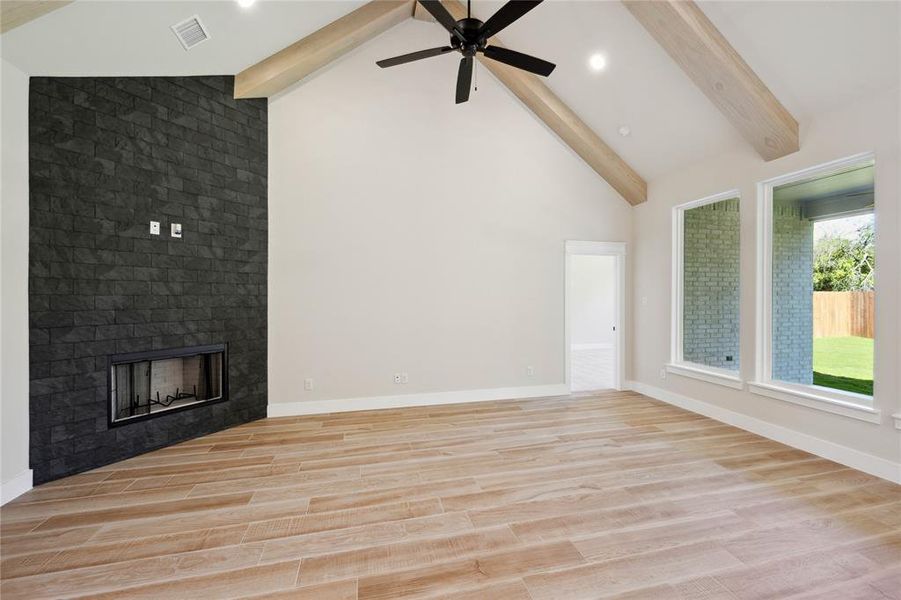 Unfurnished living room featuring ceiling fan, beam ceiling, light wood-type flooring, and a fireplace