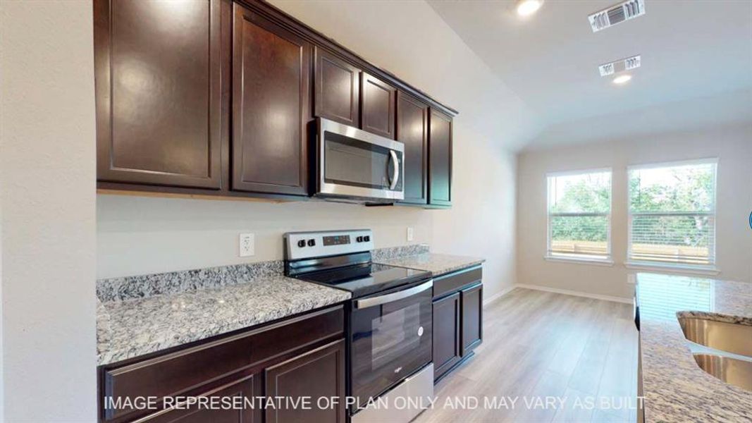 Kitchen featuring dark wood finish cabinets, stainless steel appliances, light stone countertops, light wood-style floors, and vaulted ceiling