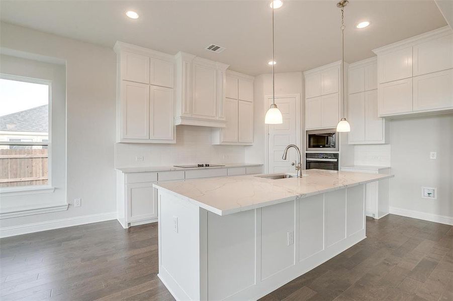 Kitchen featuring oven, a center island with sink, white cabinetry, light stone countertops, and sink