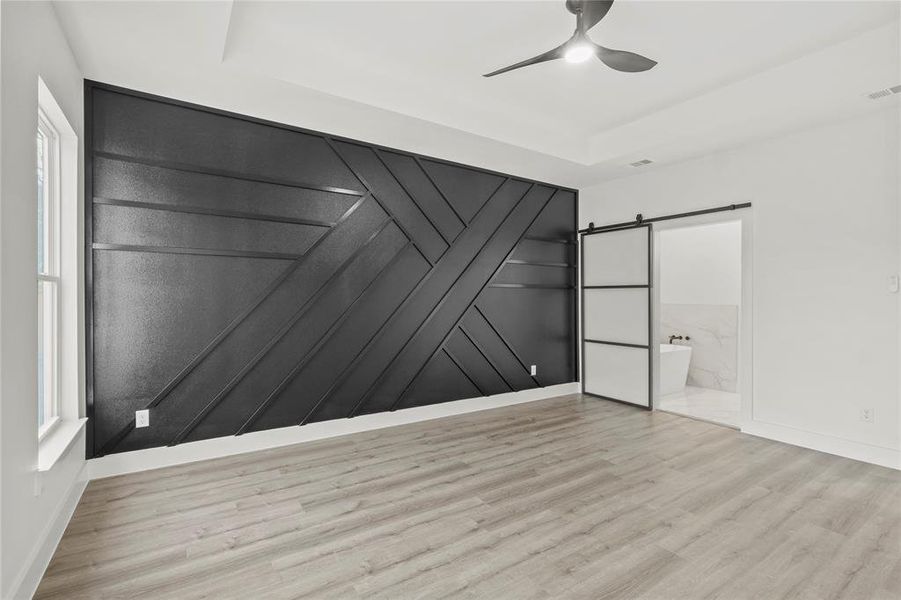 Unfurnished bedroom featuring a barn door, ceiling fan, light hardwood / wood-style flooring, and ensuite bathroom