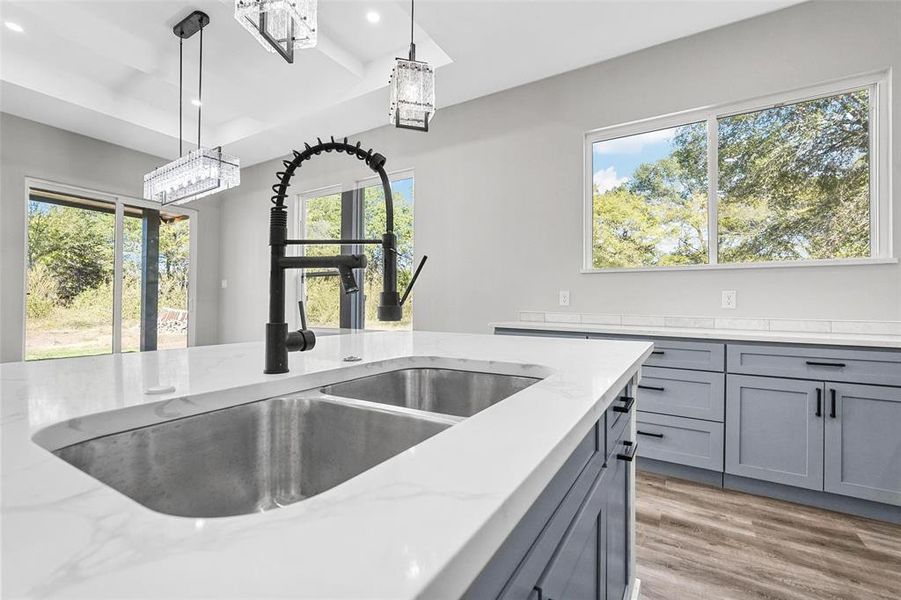 Kitchen featuring hanging light fixtures, wood-type flooring, gray cabinetry, and light stone counters