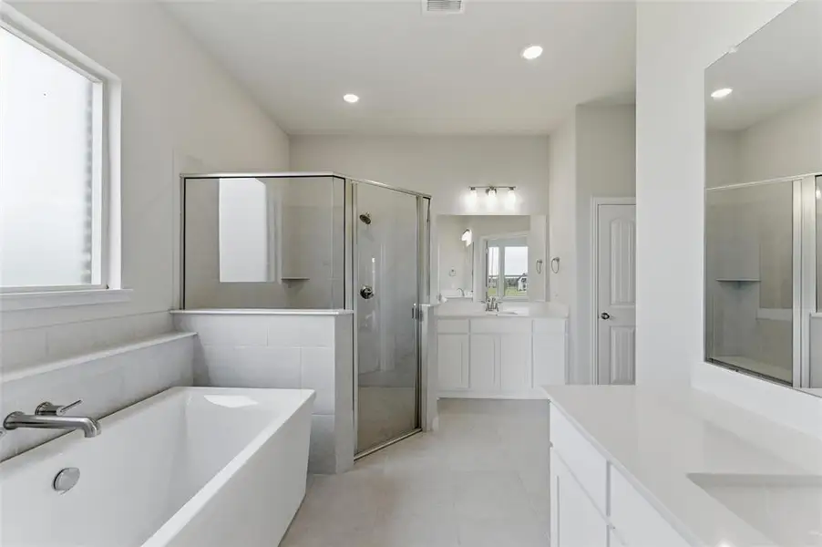 The property features a spacious bathroom with a freestanding bathtub, a glass-enclosed shower, and dual vanities with white cabinetry and light-colored countertops