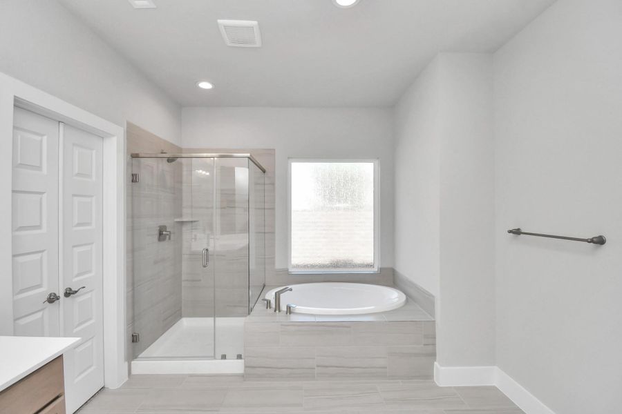 Indulge in a spa-like retreat within the confines of this primary bathroom. Delight in a spacious walk-in shower enveloped in stylish tile surround and unwind in a separate garden tub adorned with custom detailing. Sample photo of completed home with similar floor plan. Actual colors and selections may vary.