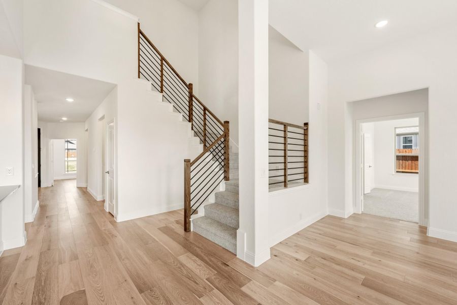 Open foyer with carpeted staircase, wood and metal railing, and light hardwood floors Open foyer with carpeted staircase, wood and metal railing, and light hardwood floors