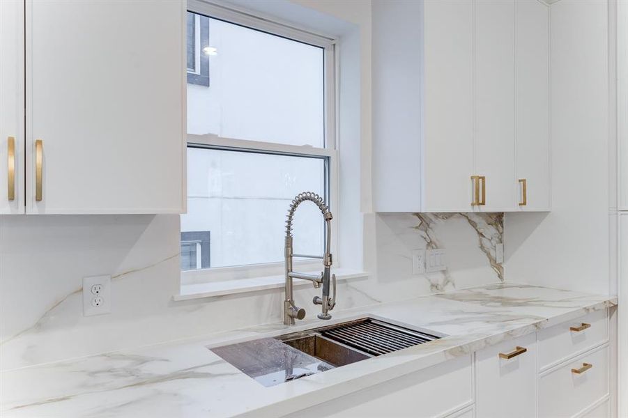 The sink area features a large window to let in natural lighting. There is a deep sink and stainless steel dishwasher.