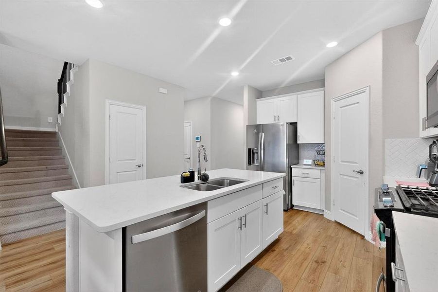 Kitchen with stainless steel appliances, white cabinetry, backsplash, light wood-style flooring, and recessed lighting Kitchen with stainless steel appliances, white cabinetry, backsplash, light wood-style flooring, and recessed lighting