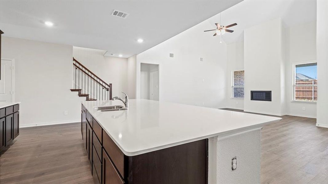 Spacious open-concept interior featuring a large kitchen island with integrated sink, dark wood-finish cabinetry, wood-finish flooring, and a two-story living area with a fireplace