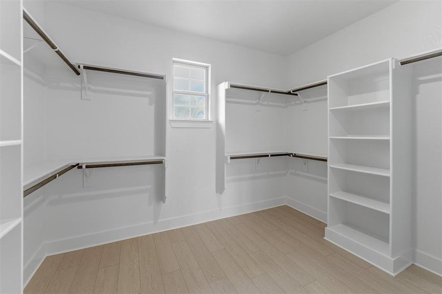 Spacious walk-in closet featuring light wood-finish flooring and extensive built-in storage Spacious walk-in closet featuring light wood-finish flooring and extensive built-in storage