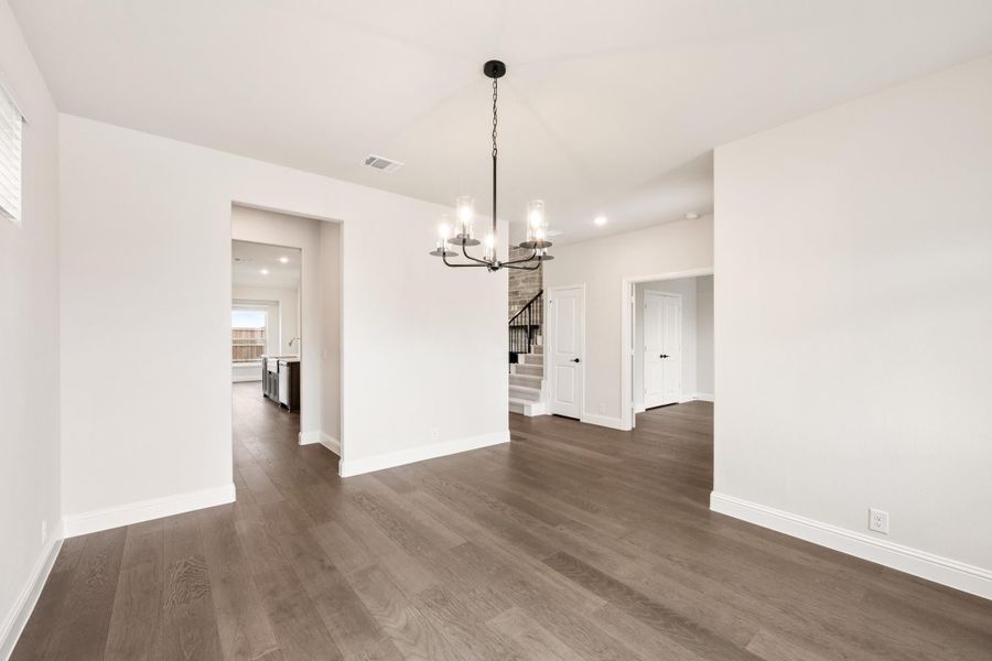 Empty dining room with dark hardwood floors, white walls, and a black chandelier overhead