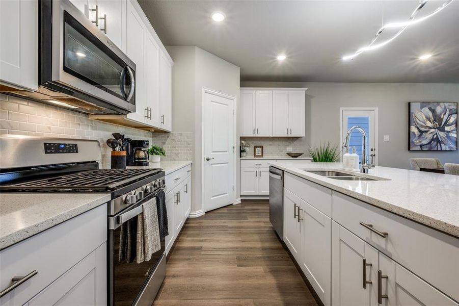 Kitchen with appliances with stainless steel finishes, white cabinetry, decorative backsplash, light stone countertops, and recessed lighting Kitchen with appliances with stainless steel finishes, white cabinetry, decorative backsplash, light stone countertops, and recessed lighting