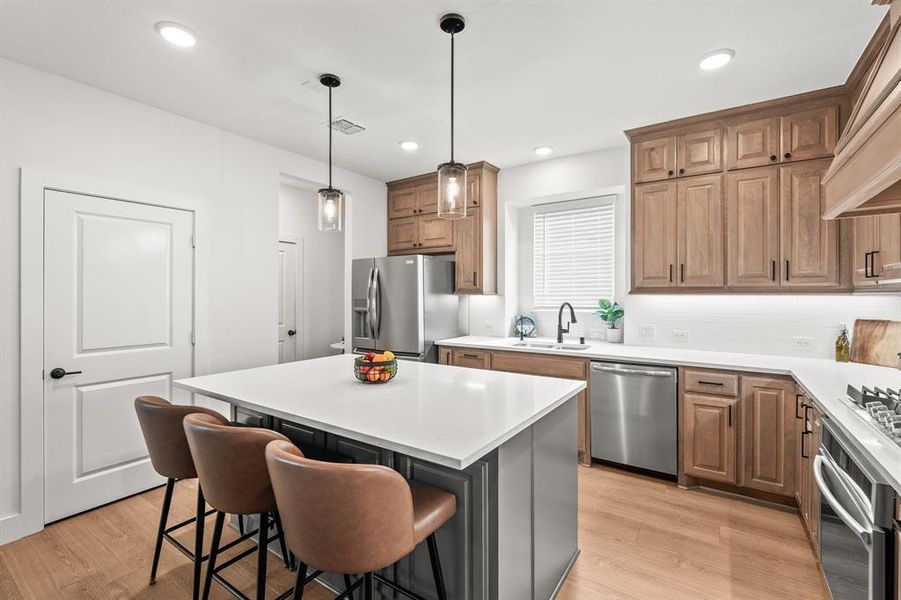 Kitchen with light wood finished floors, stainless steel appliances, decorative light fixtures, a kitchen breakfast bar, and recessed lighting Kitchen with light wood finished floors, stainless steel appliances, decorative light fixtures, a kitchen breakfast bar, and recessed lighting