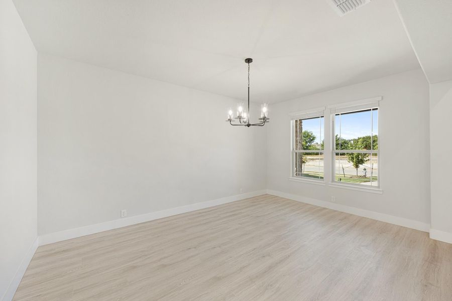 Empty dining room with light wood floors, white walls, chandelier, and double window