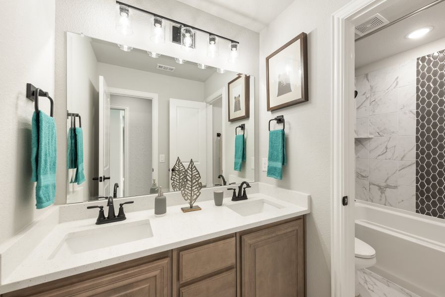 Bathroom with double sink vanity, wood cabinets, and tiled shower with hexagon accent wall