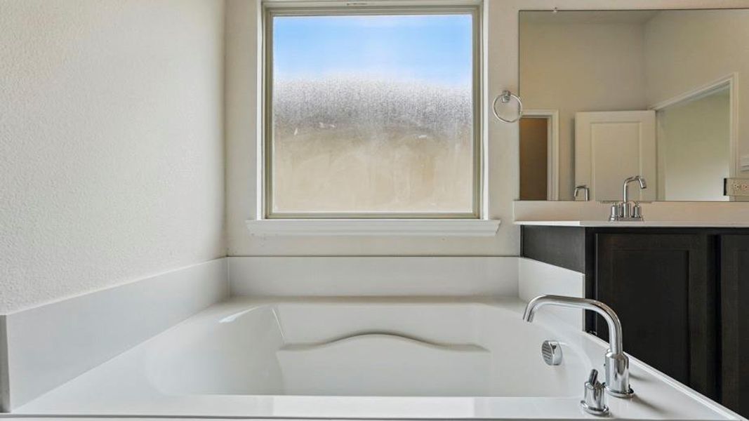 Built-in soaking tub with polished chrome fixtures, surrounded by white countertops and a privacy window