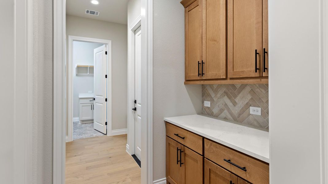 Bar area featuring brown cabinets, backsplash, light wood-style floors, and light stone countertops