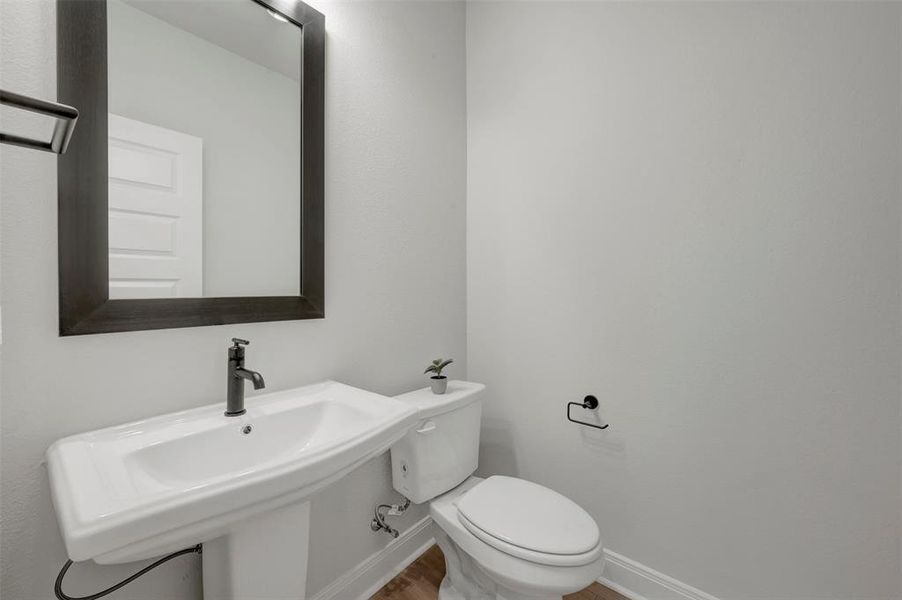 Modern bathroom featuring a pedestal sink with a matte black faucet, framed mirror, and wood-finish flooring