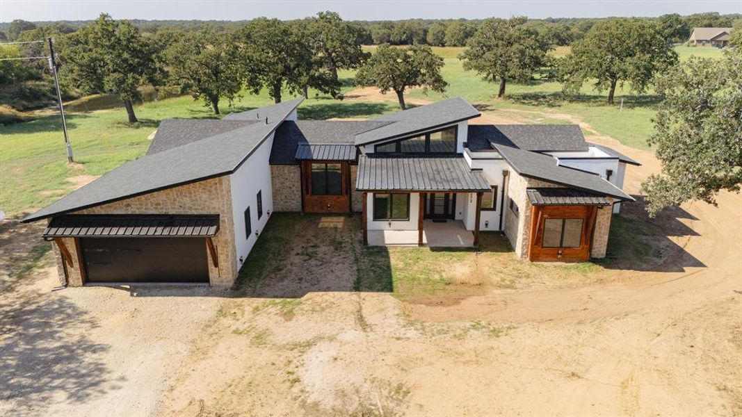 View of front of property with a metal roof, a standing seam roof, dirt driveway, a patio area, and a front lawn