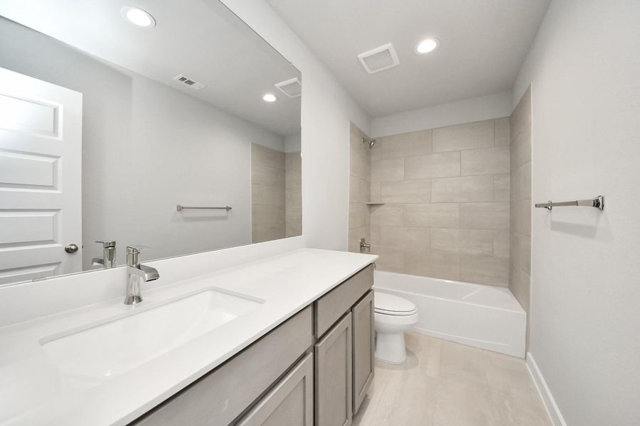 Secondary bath features tile flooring, bath/shower combo with tile surround, light stained wood cabinets, beautiful light countertop. Sample photo of completed home with similar floor plan. Actual colors and selections may vary. Secondary bath features tile flooring, bath/shower combo with tile surround, light stained wood cabinets, beautiful light countertop. Sample photo of completed home with similar floor plan. Actual colors and selections may vary.