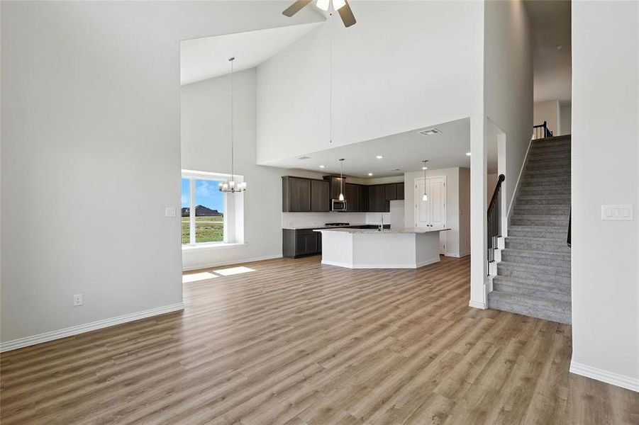 Unfurnished living room with a high ceiling, light wood-style flooring, stairway, ceiling fan, and a chandelier Unfurnished living room with a high ceiling, light wood-style flooring, stairway, ceiling fan, and a chandelier
