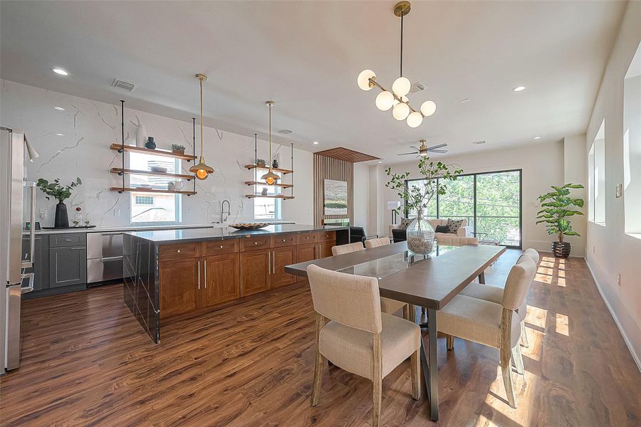 This is a spacious and modern open-plan kitchen and dining area featuring sleek wooden cabinetry, stainless steel appliances, stylish pendant lighting, and large windows that provide ample natural light. The warm hardwood floors complement the neutral color palette, creating an inviting space for both cooking and entertaining. This is a spacious and modern open-plan kitchen and dining area featuring sleek wooden cabinetry, stainless steel appliances, stylish pendant lighting, and large windows that provide ample natural light. The warm hardwood floors complement the neutral color palette, creating an inviting space for both cooking and entertaining.
