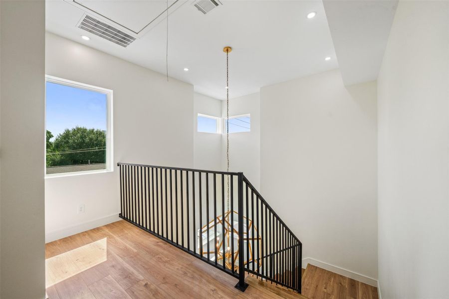 Bright stairwell with modern black railing, wood flooring, and ample natural light from large windows. Clean, minimalist design with recessed lighting.
