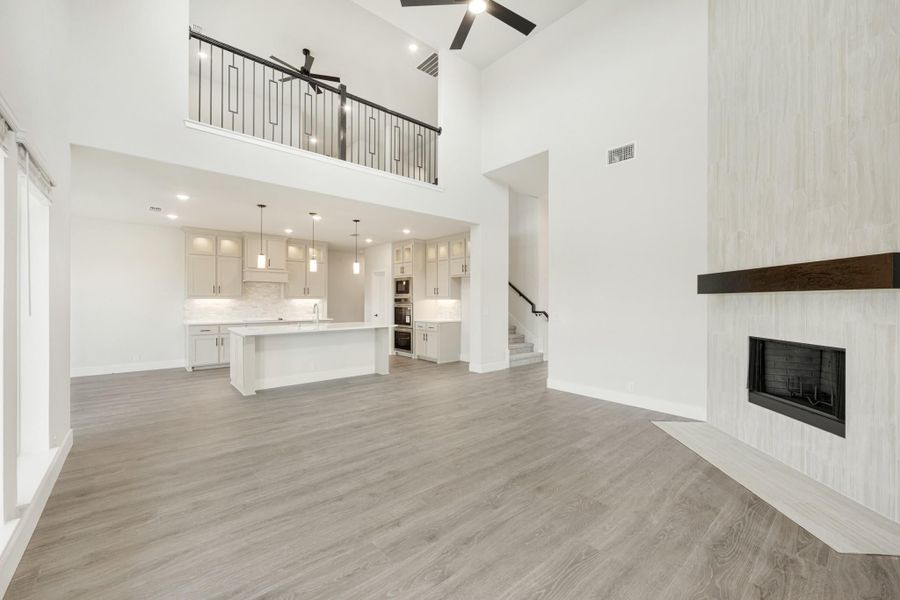 Open living area with two-story ceiling, fireplace, and kitchen with island visible in background
