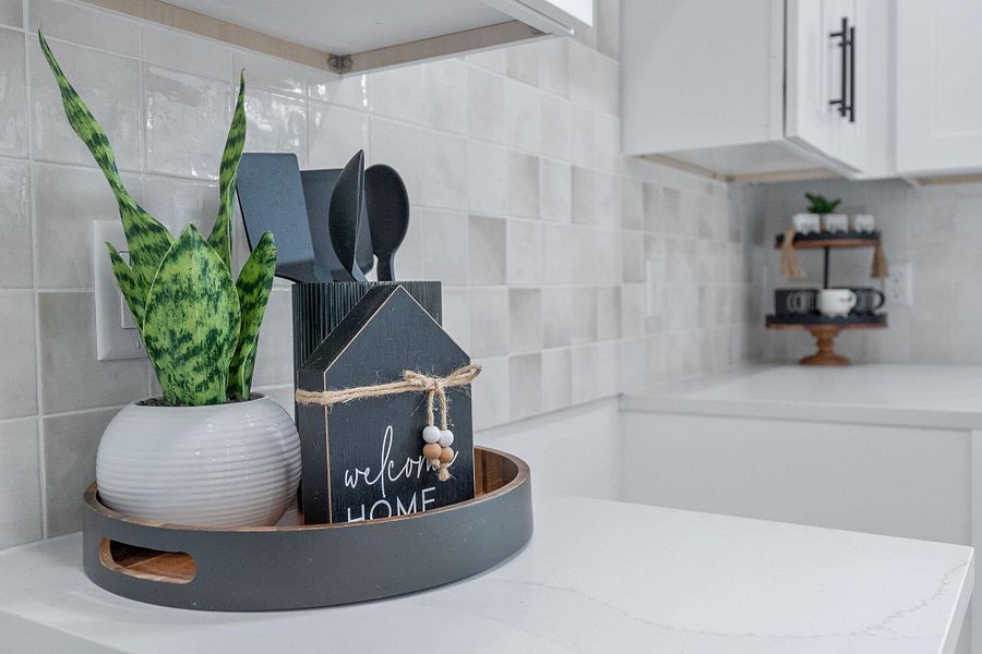 Kitchen view of decorative backsplash, white cabinetry, and light countertops
