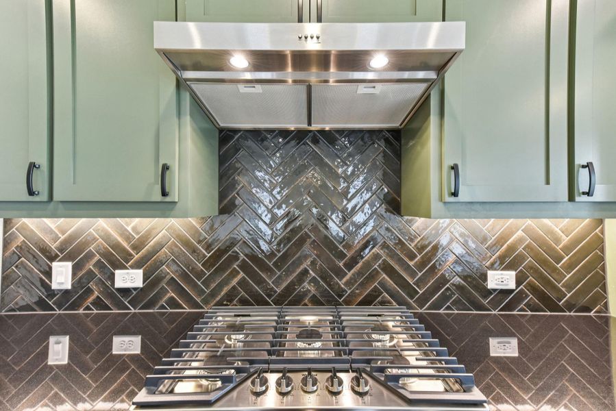 Kitchen view of range hood, green cabinets, stainless steel gas cooktop, and decorative backsplash