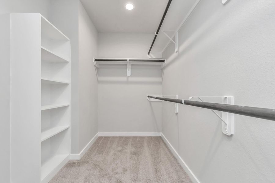 Walk-in closet that epitomizes luxury and practicality. This generously sized space features built-in shelving, offering abundant room for impeccable organization. High ceilings and recessed lighting create a bright and welcoming ambiance. Sample photo of completed home with similar floor plan. Actual colors and selections may vary.