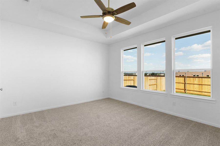 Carpeted empty room featuring a tray ceiling and a ceiling fan