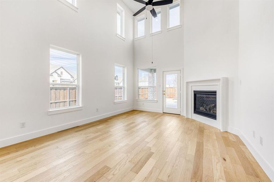 Unfurnished living room with light wood-type flooring, a glass covered fireplace, a ceiling fan, and a high ceiling