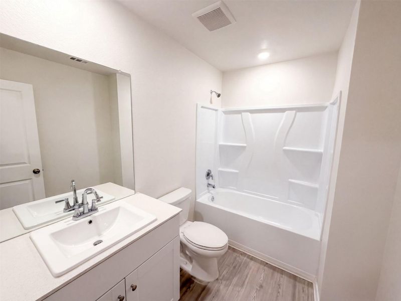 An integrated tub and shower combination sits adjacent to a white vanity with wood-look flooring.
