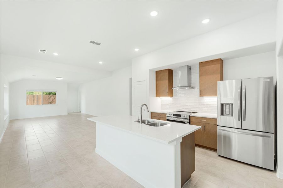 Open kitchen with center island, stainless steel appliances, wood cabinets, and white countertops opening to living area
