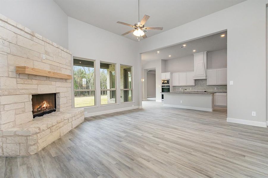 Unfurnished living room featuring ceiling fan, a fireplace, light hardwood / wood-style floors, and a high ceiling